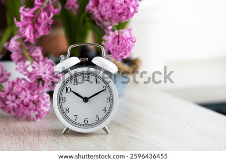 Daylight spring saving time concept. white alarm clock changing from winter to summer time. Turn time forward. Pink fresh springtime flowers hyacinth on background. Home gardening, leisure, hobby