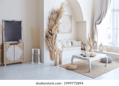 daylight through a huge panoramic window illuminates the cozy oriental interior of the room in beige colors with wicker furniture and authentic elements - Shutterstock ID 1999772894
