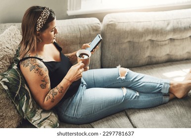 Days off are for doing just this. a young woman using a smartphone and having coffee on the sofa at home. - Powered by Shutterstock