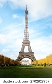 Daytime view of the Eiffel Tower in Paris with autumn trees and blue sky.