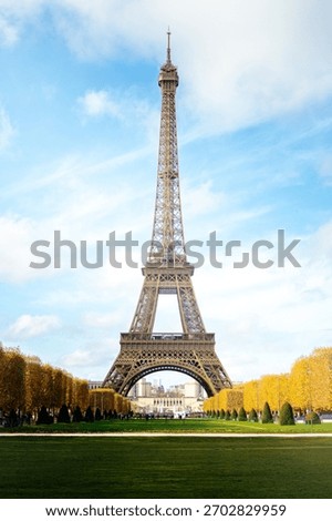 Daytime view of the Eiffel Tower in Paris with autumn trees and blue sky.