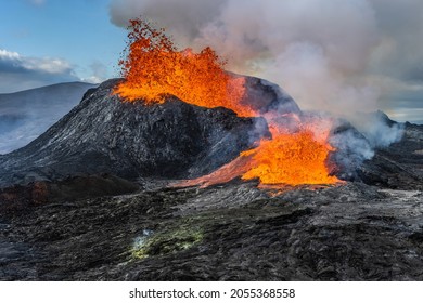 Daytime volcanic eruption on Reykjanes peninsula. Lava shoots up from the crater above. Crater from Fagradalsfjall volcano in Iceland in GeoPark. Clouds and steam in the sky.  - Shutterstock ID 2055368558