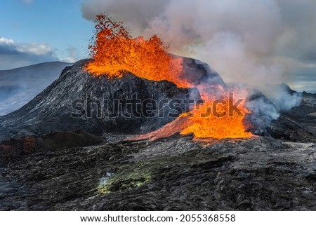 Daytime volcanic eruption on Reykjanes peninsula. Lava shoots up from the crater above. Crater from Fagradalsfjall volcano in Iceland in GeoPark. Clouds and steam in the sky. 