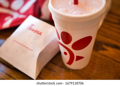 Dayton, OH- Mar 16, 2020; Chick Fil A Cup With Other Food Items In Background. Boxes And Bags Of Trash Following Meal. Reflection On Wooden Table