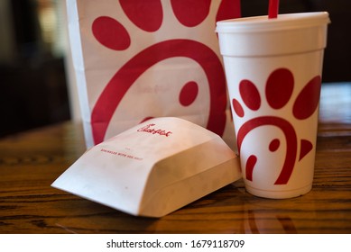 Dayton, OH- Mar 16, 2020; Chick Fil A Box With Other Food Items In Background. Boxes And Bags Of Trash Following Meal. Reflection On Wooden Table