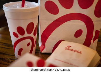 Dayton, OH- Mar 16, 2020; Chick Fil A Box With Other Food Items In Background. Boxes And Bags Of Trash Following Meal. Reflection On Wooden Table