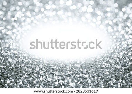 A dazzling abstract background featuring shimmering silver glitter particles and a bright, glowing light emanating from the center.