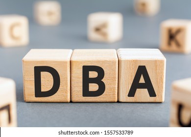 DBA - acronym from wooden blocks with letters, DataBase Administrator or doing business as abbreviation DBA concept, random letters around, gray background