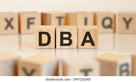 DBA - acronym from wooden blocks with letters, DataBase Administrator or doing business as abbreviation DBA concept, random letters around, yelllow background