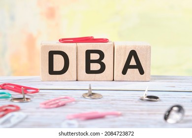 DBA text on wooden cubes next to stationery buttons and paper clips.