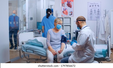 Dcotor checking old retired woman heart related problems during pandemic in modern private clinic or hospital. Patient and medical stuff wearing masks for protection against COVID-19. Medical