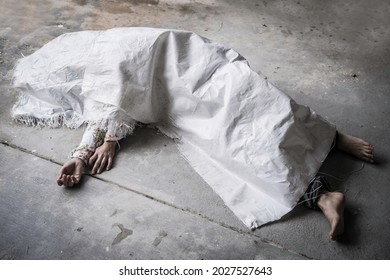 Dead body of a barefoot asian woman wrapped in a sack and abandoned on the concret floor. 