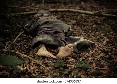 Dead Body Of A Barefoot Caucasian Boy Wrapped In A Blanket And Abandoned On The Ground In The Forest