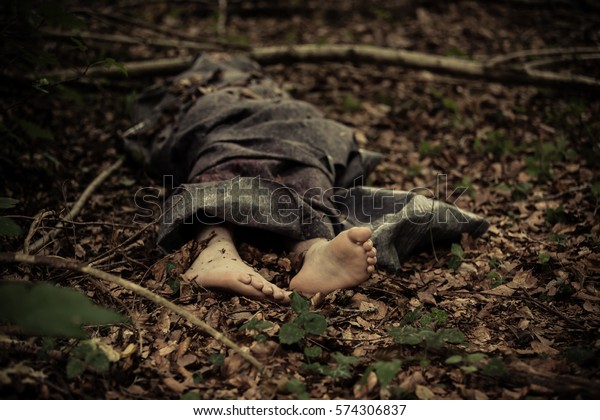 Cuerpo muerto de un niño caucásico descalzo envuelto en una manta y abandonado en el suelo en el bosque