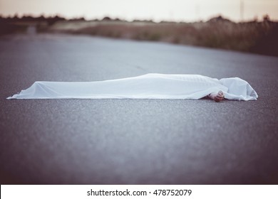 Dead Body With Hand Sticking Out From Under White Sheet In Middle Of Road With Copy Space