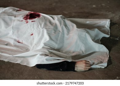 Dead Body Of Killed Person Covered By White Sheet Lying On Asphalt On Crime Scene In Parking Area Or Somwhere Else In The Street