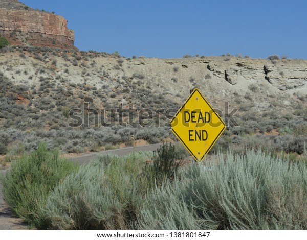 Dead End sign in the road with cliffs and bushes\
along the road.