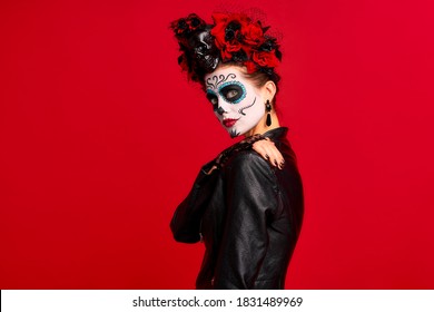 Dead gir with sugar skull makeup with a wreath of flowers on her head and skull, standing in profile, isolated on red background. concept of Halloween or La Calavera Catrina.