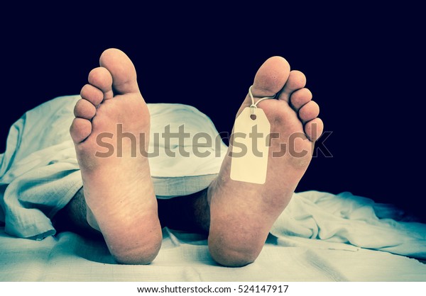The dead man\'s body with blank tag\
on feet under white cloth in a morgue - retro\
style