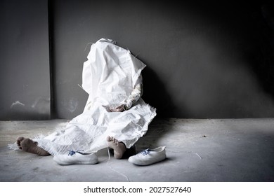 Dead person die in sitting position againt dark brown wall and concret floor with blurred shoes and bare foot was wrapped by white sack with copy space.