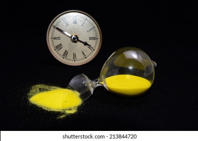 Deadline Concept Broken Hourglass with Yellow Sand on Black Background