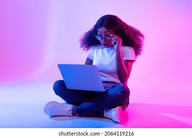 Deadline concept. Full length of surprised black woman using laptop computer, opening mouth in shock in neon light. Stressed African American lady working online, making error in project