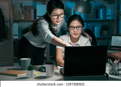 Deadline Technology And People Concept. Creative Startup Business Team With Laptop Computer Working Together Late At Night Office. Two Young Asian Woman Colleagues Talking Point On Screen Smiling.