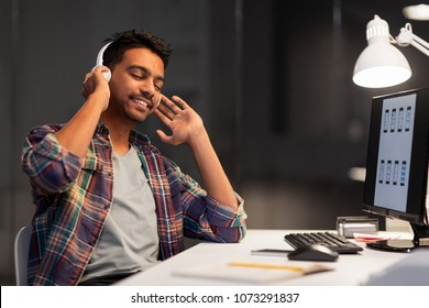 Deadline, Technology And People Concept - Happy Creative Man With Headphones And Computer Listening To Music At Night Office