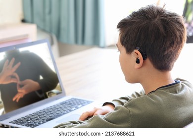 Deaf teenager boy Wearing Hearing Aid using Laptop. Disable student with disabilities deafness distancing learning online from home making communication hands language with teacher via VDO call.