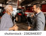 Dealer and farmer in tractor workshop talking about service and maintenance.