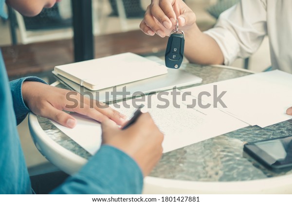 dealer salesman giving
car key to new owner. client signing insurance document or rental
car lease form