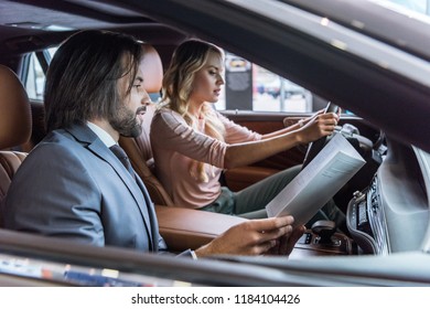 dealership salon seller and female customer sitting in car in auto salon