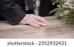 Death, funeral and hand on coffin in mourning, family at service in graveyard or church for respect. Flowers, loss and people at wood casket in cemetery with memory, grief and sadness at grave burial