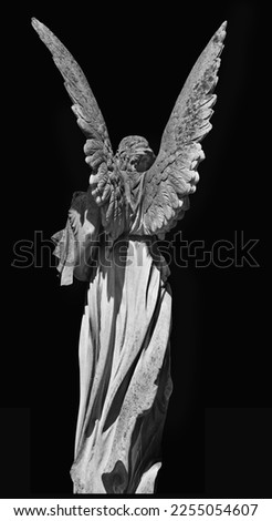 Death. Rear view of angel as symbol of end of life. Ancient stone statue against black background.. 
