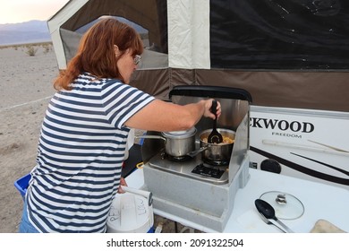 Death Valley, California, March12, 2021: Camping In Stovepipe Wells Death Valley, California, With A Pop-Up Trailer At Sunset With A Mature Woman Outside The Trailer Making Dinner At Sunset