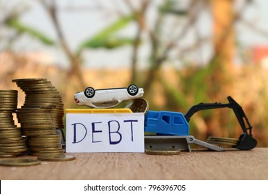 Debt Car Concept, White Miniature Vehicle Falls On Truck With Rolls Of Unsecured Gold Coin Money On Wood Table In Blur Natural Tree