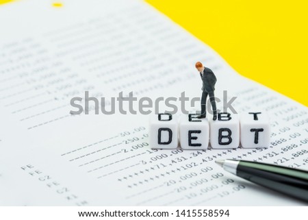 Debt, financial obligation or money to pay back to creditor concept, miniature businessman standing and thinking on cube blocks with alphabet building the word Debt on bank account statement with pen.