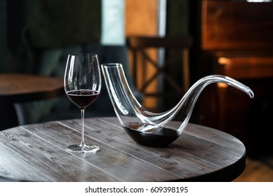 Decanter with red wine and glass on wooden table in interior. Free space for text. Still life style