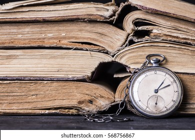 Decaying clock on the background of old shabby wise books. - Shutterstock ID 568756867