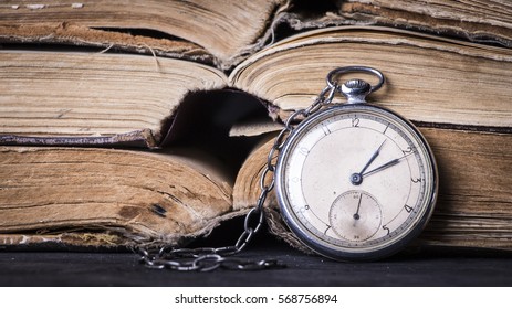 Decaying clock on the background of old shabby wise books. - Shutterstock ID 568756894