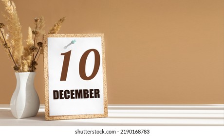 december 10. 10th day of month, calendar date.White vase with dead wood next to cork board with numbers. White-beige background with striped shadow. Concept of day of year, time planner, winter month.