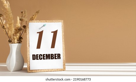 december 11. 11th day of month, calendar date.White vase with dead wood next to cork board with numbers. White-beige background with striped shadow. Concept of day of year, time planner, winter month.
