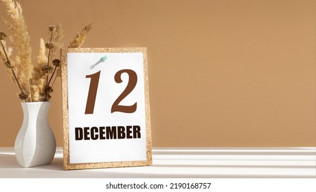 december 12. 12th day of month, calendar date.White vase with dead wood next to cork board with numbers. White-beige background with striped shadow. Concept of day of year, time planner, winter month.