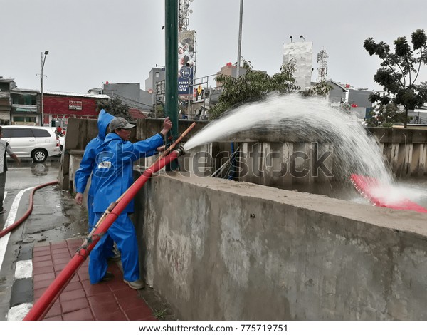 December\
12, 2017, Jakarta, Indonesia : Asian worker  controlling the hose \
spraying  high  pressure water into the\
river.