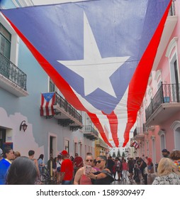 December 13, 2019, San Juan, Puerto Rico. A Pair Of Girls Take A Selfie Beneath A Huge Puerto Rican Flag That Is Draped  Above Calle De La Fortaleza In San Juan, Puerto Rico.