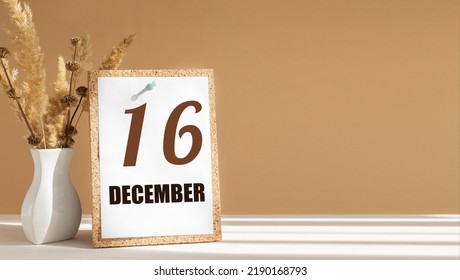 december 16. 16th day of month, calendar date.White vase with dead wood next to cork board with numbers. White-beige background with striped shadow. Concept of day of year, time planner, winter month.