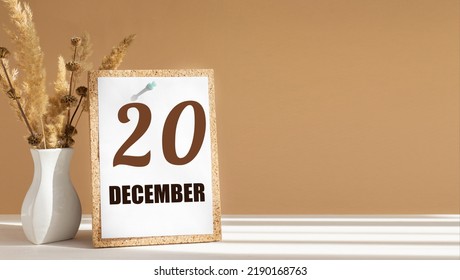 december 20. 20th day of month, calendar date.White vase with dead wood next to cork board with numbers. White-beige background with striped shadow. Concept of day of year, time planner, winter month.