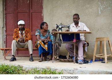 December, 2019, Africa, Uganda, A Man Sews On An Old Mechanical Sewing Machine And Two People Waiting