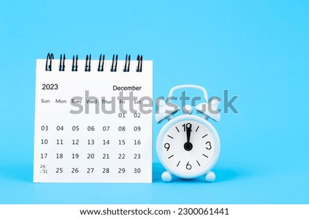 December 2023 desk calendar and alarm clock on blue color background.