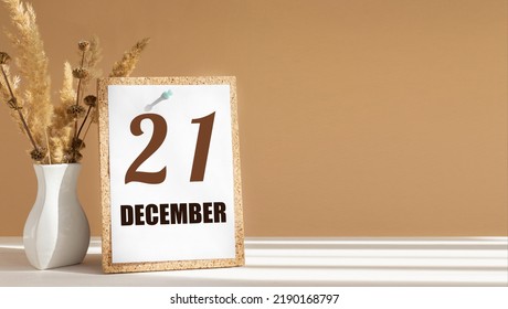 december 21. 21th day of month, calendar date.White vase with dead wood next to cork board with numbers. White-beige background with striped shadow. Concept of day of year, time planner, winter month.